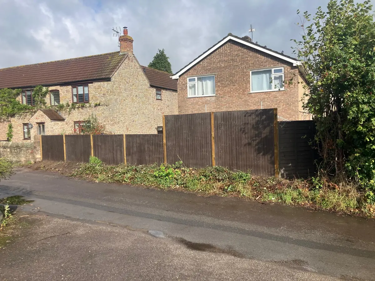 Close board fencing replaced along a roadside boundary in front of stone houses