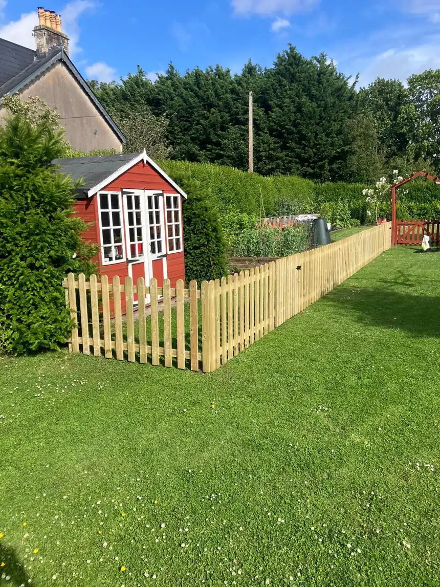Timber picket fencing running along a lawn beside a red summer house